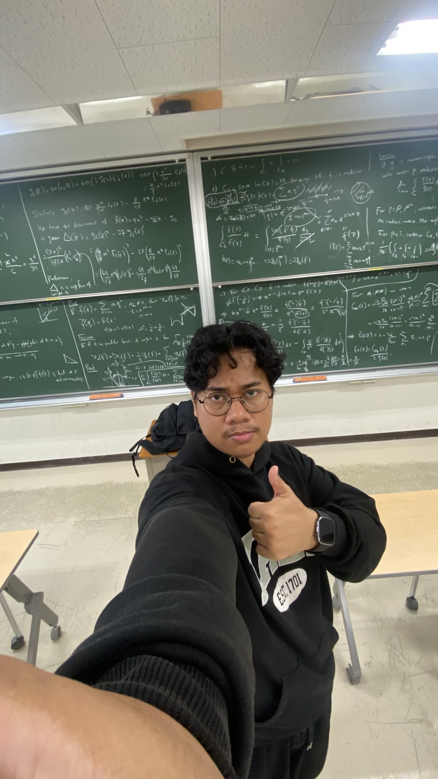 Hasbi giving a thumbs up in front of blackboards full of modular forms calculations